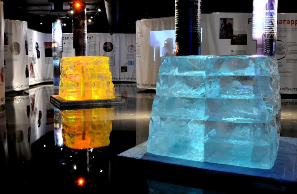 Image showing an exhibition room with to large ice blocks lit in blue and yellow, in the center.